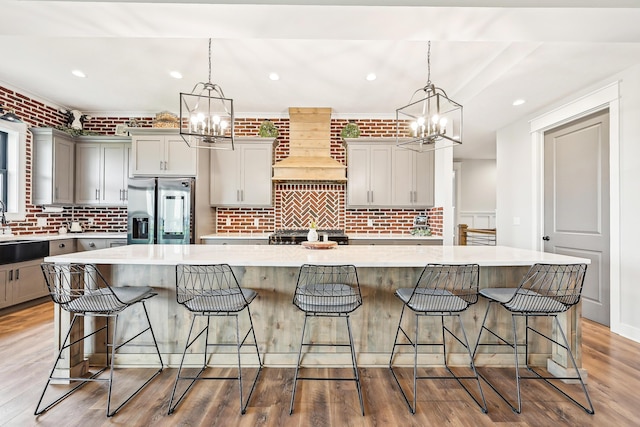 kitchen featuring an inviting chandelier, gray cabinetry, custom range hood, and stainless steel refrigerator with ice dispenser