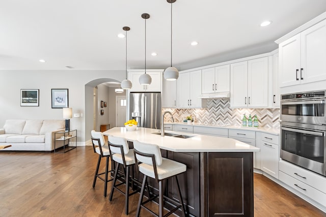 3325 Strickland Dr, New Albany, OH 43054 - kitchen featuring light countertops, a sink, arched walkways, decorative backsplash, and appliances with stainless steel finishes