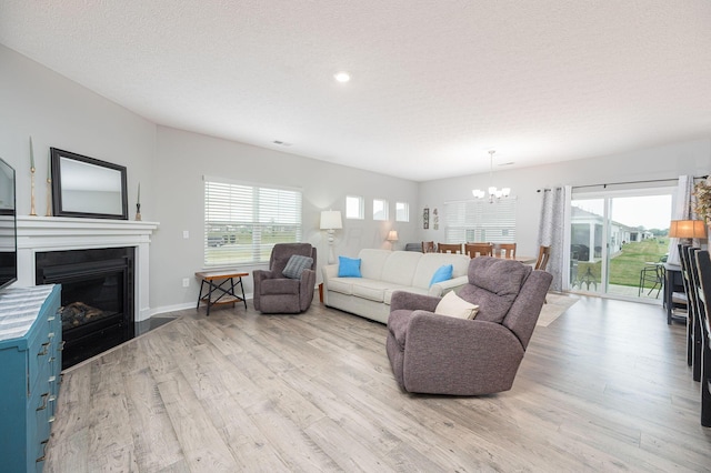 458 Madison Way, Plain City, OH 43064 - living area featuring a textured ceiling, light wood finished floors, baseboards, a glass covered fireplace, and a notable chandelier