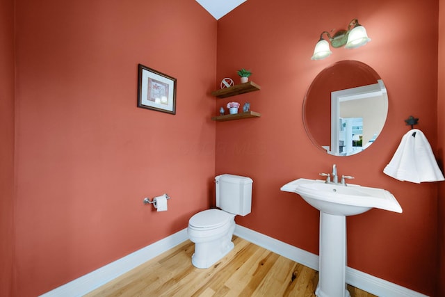 half bath featuring a sink, toilet, wood finished floors, and baseboards