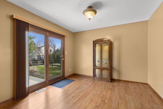 empty room with baseboards, light wood finished floors, visible vents, and plenty of natural light