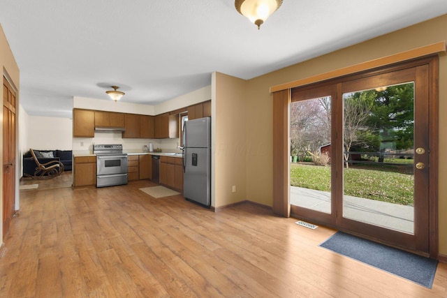 kitchen with light countertops, light wood-type flooring, under cabinet range hood, stainless steel appliances, and baseboards