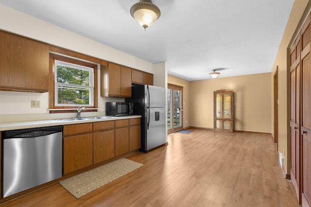 kitchen featuring light countertops, a sink, brown cabinetry, stainless steel appliances, and light wood-style floors