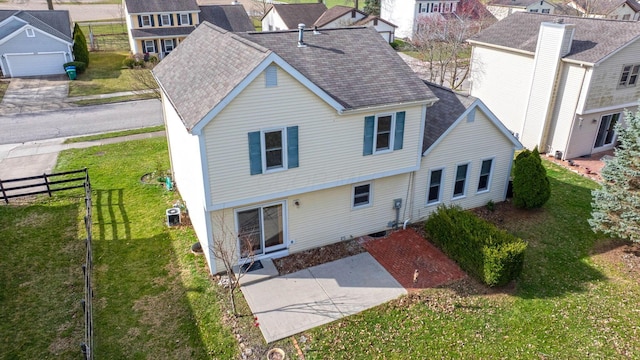 back of property with a shingled roof, fence, and a yard