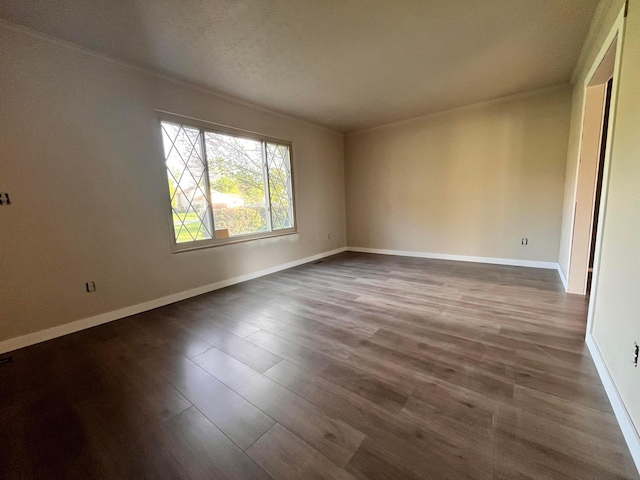 spare room with wood finished floors, crown molding, and baseboards
