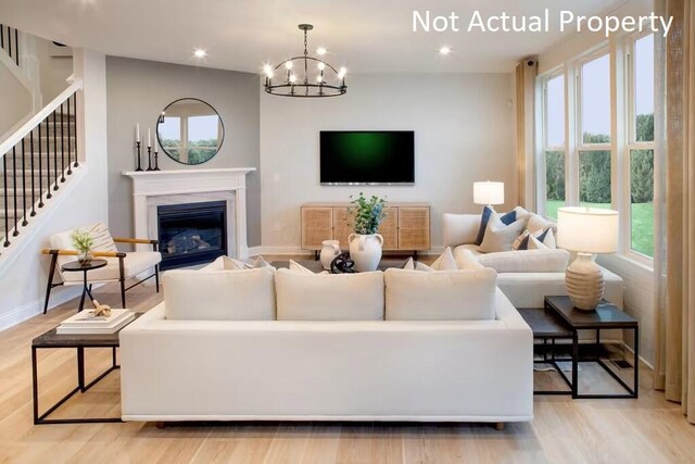 living room featuring baseboards, a glass covered fireplace, an inviting chandelier, light wood-style floors, and stairway