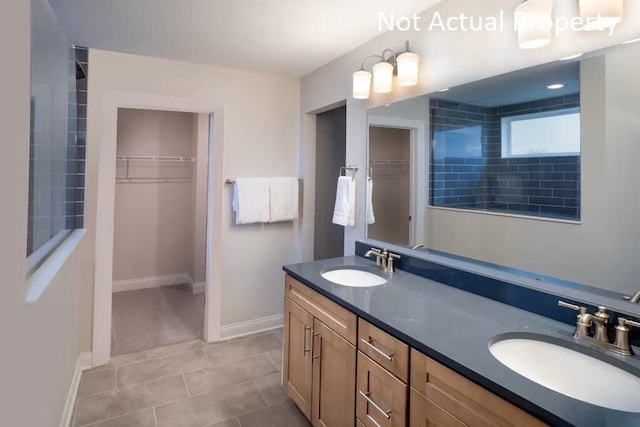 bathroom featuring tile patterned flooring, a walk in closet, a sink, and double vanity