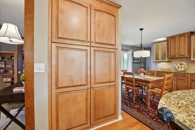 397 E Schrock Rd, Westerville, OH 43081 - kitchen with decorative backsplash, light stone counters, pendant lighting, light wood-style flooring, and glass insert cabinets