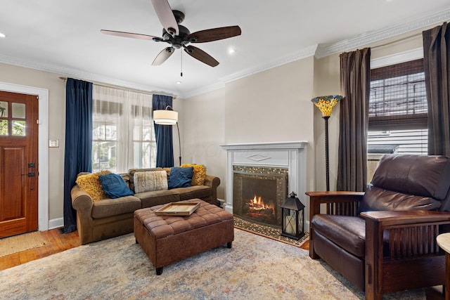 living area with wood finished floors, a fireplace with flush hearth, crown molding, ceiling fan, and recessed lighting