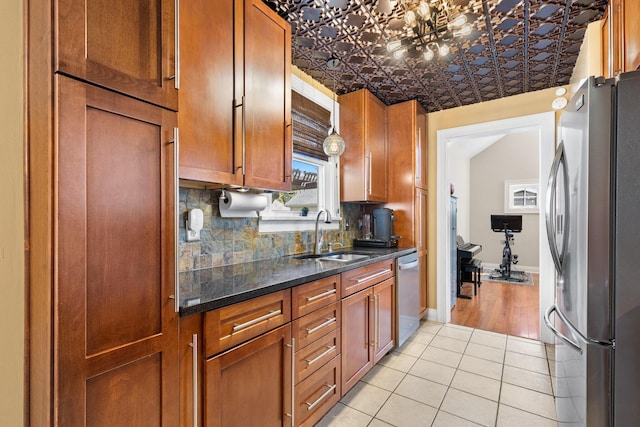 kitchen with a sink, stainless steel appliances, brown cabinets, light tile patterned flooring, and backsplash