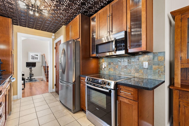 kitchen featuring stainless steel appliances, tasteful backsplash, brown cabinets, glass insert cabinets, and baseboards
