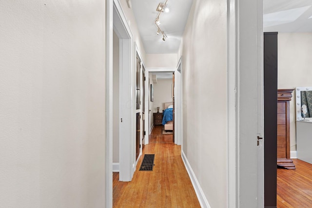 hallway with baseboards, visible vents, and light wood-type flooring