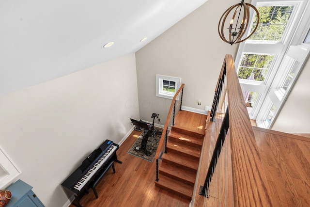 staircase featuring an inviting chandelier, wood finished floors, baseboards, and high vaulted ceiling