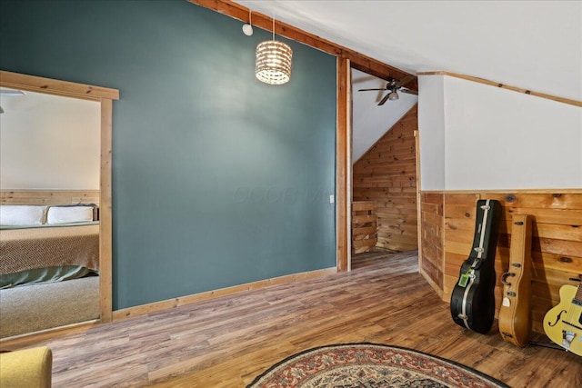 bonus room featuring lofted ceiling with beams, wood walls, ceiling fan, and wood finished floors