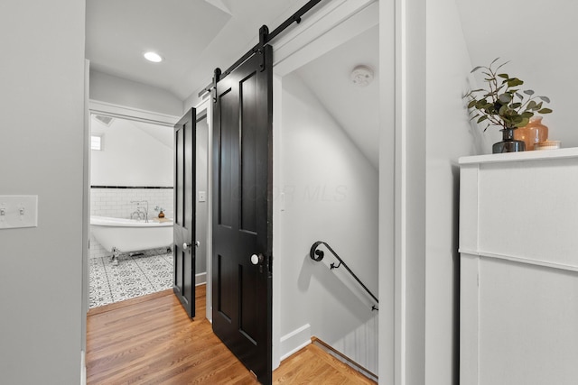 corridor featuring a barn door, recessed lighting, an upstairs landing, light wood-type flooring, and vaulted ceiling