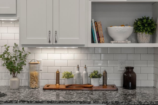 interior details with decorative backsplash, dark stone counters, and white cabinets
