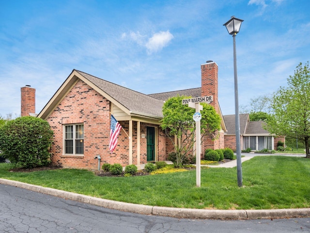 view of front facade with brick siding, a chimney, a shingled roof, and a front lawn