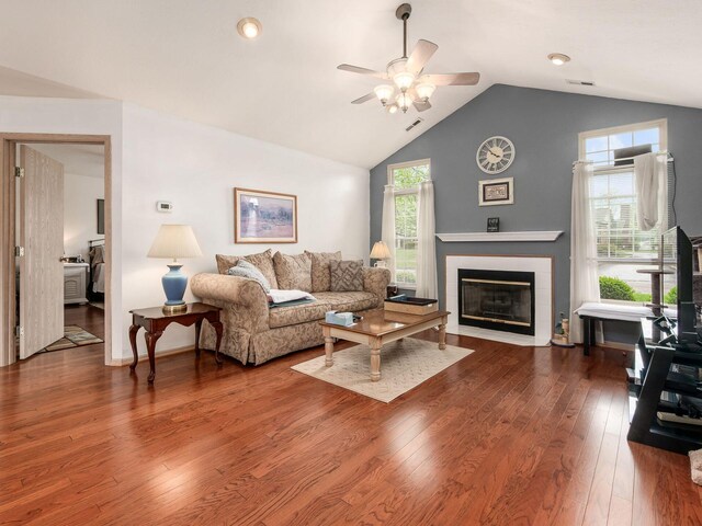 living area featuring ceiling fan, visible vents, a tiled fireplace, wood finished floors, and vaulted ceiling