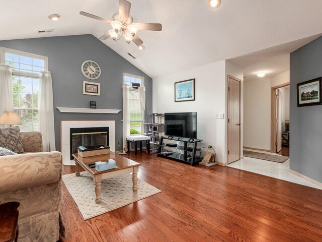 living room with ceiling fan, visible vents, a fireplace, wood finished floors, and lofted ceiling