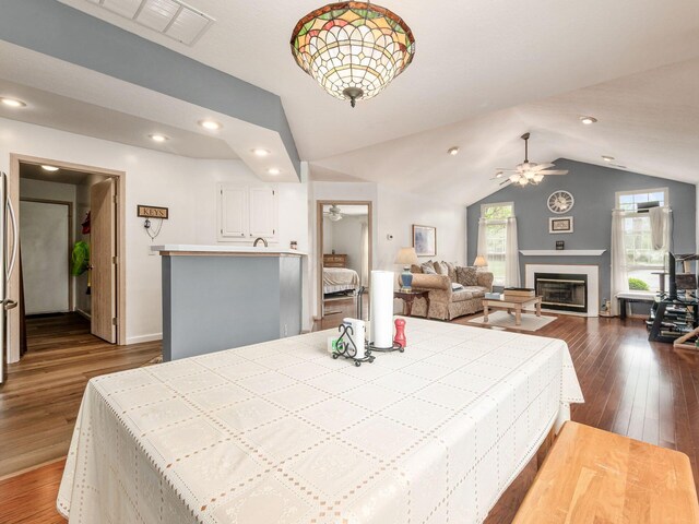 dining space featuring dark wood-style flooring, a glass covered fireplace, lofted ceiling, baseboards, and ceiling fan