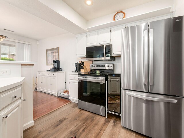 kitchen with appliances with stainless steel finishes, visible vents, wood finished floors, and white cabinetry