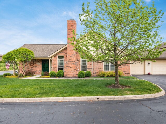 view of front of house featuring brick siding, a garage, aphalt driveway, a front yard, and a chimney