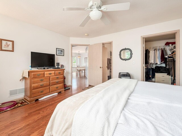 bedroom with a ceiling fan, visible vents, wood finished floors, and a spacious closet