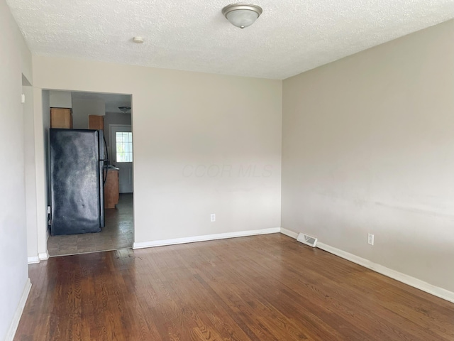 unfurnished room with visible vents, a textured ceiling, baseboards, and dark wood-style floors