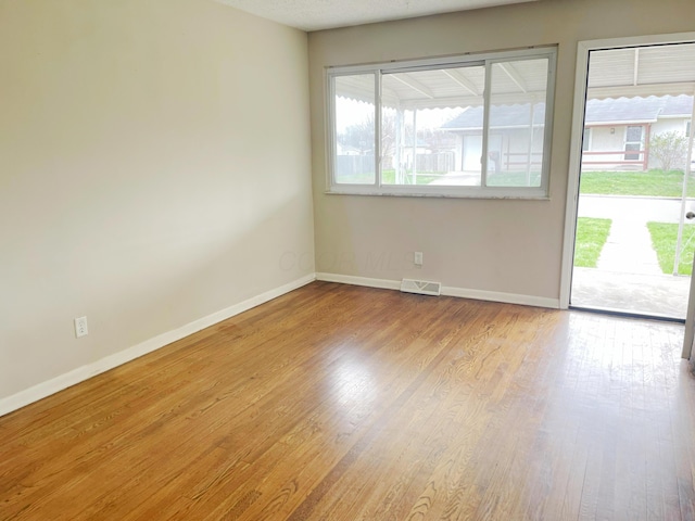 spare room with baseboards, visible vents, and wood finished floors