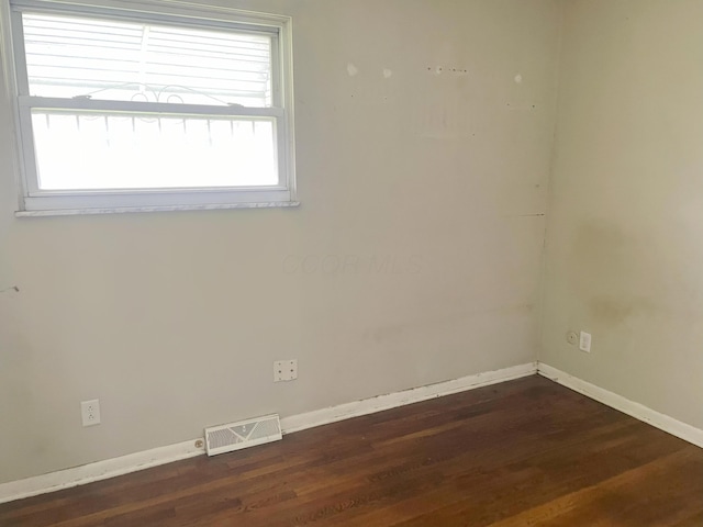 unfurnished room with baseboards, visible vents, and dark wood finished floors