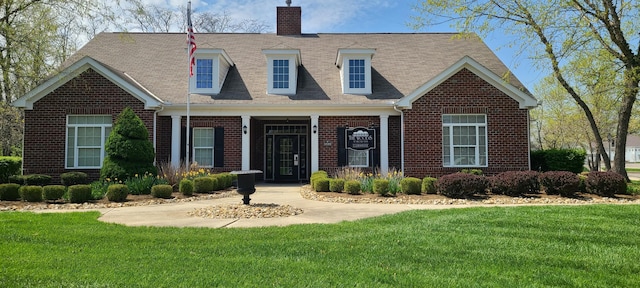 new england style home with a front lawn, a chimney, brick siding, and roof with shingles
