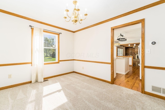 spare room with an inviting chandelier, ornamental molding, visible vents, baseboards, and carpet