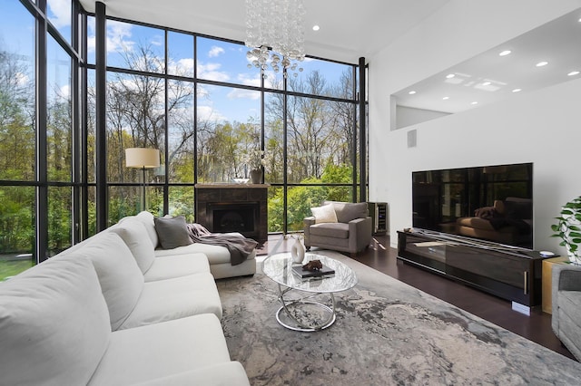 living area featuring a towering ceiling, an inviting chandelier, a wall of windows, wood finished floors, and a fireplace