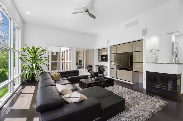 living room with a fireplace with flush hearth, visible vents, ceiling fan, and dark wood-style flooring