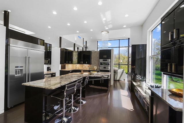 kitchen with dark cabinets, a large island, stainless steel appliances, backsplash, and dark wood-style flooring