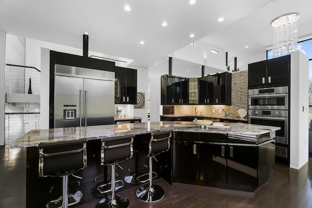 kitchen featuring dark cabinets, tasteful backsplash, dark wood-type flooring, and appliances with stainless steel finishes