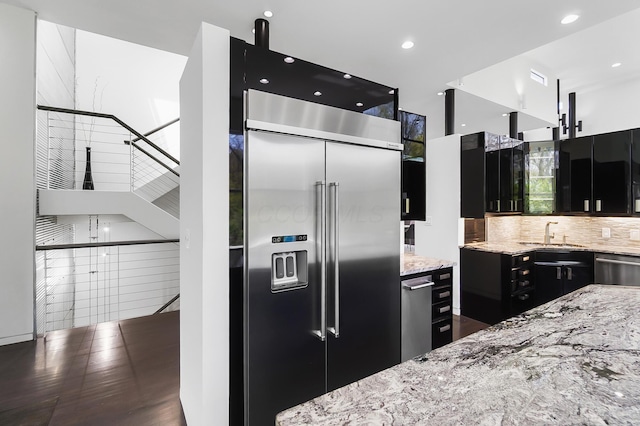 kitchen featuring light stone counters, a sink, decorative backsplash, appliances with stainless steel finishes, and dark cabinets