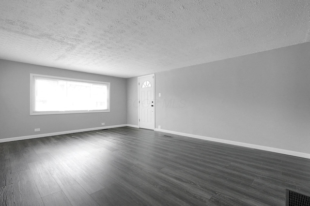 unfurnished living room with a textured ceiling, baseboards, dark wood finished floors, and visible vents