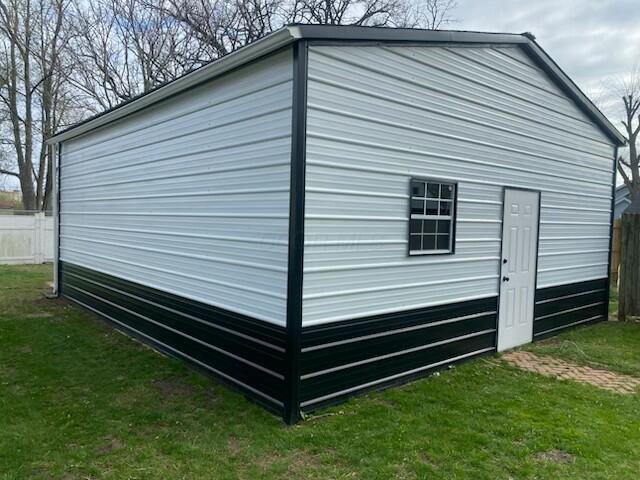 view of side of property with a detached garage, fence, an outdoor structure, and a lawn
