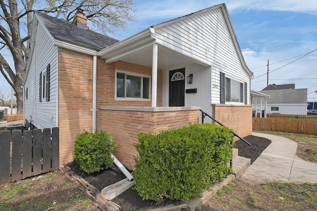 bungalow-style house featuring brick siding, fence, and a chimney