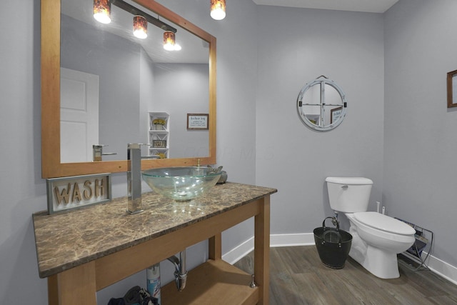 half bath featuring baseboards, toilet, wood finished floors, and a sink