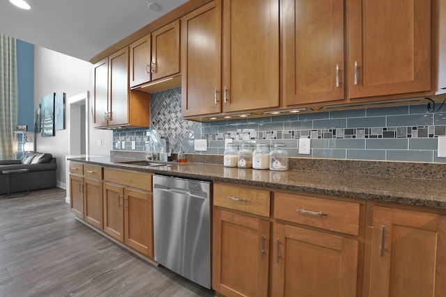 kitchen with brown cabinets, wood finished floors, stainless steel dishwasher, a sink, and tasteful backsplash