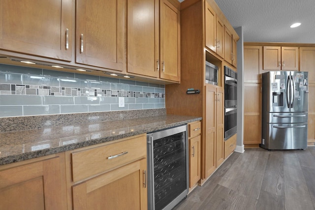 kitchen with wood finished floors, beverage cooler, backsplash, and appliances with stainless steel finishes