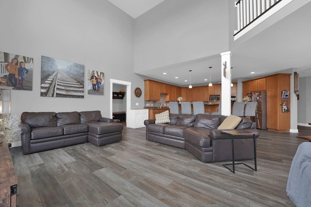 living room featuring a towering ceiling, baseboards, wood finished floors, and recessed lighting