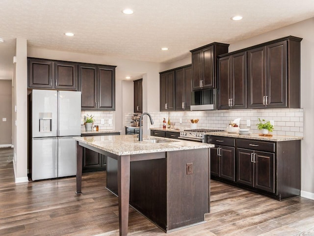 kitchen with wood finished floors, white fridge with ice dispenser, a sink, light stone counters, and gas range