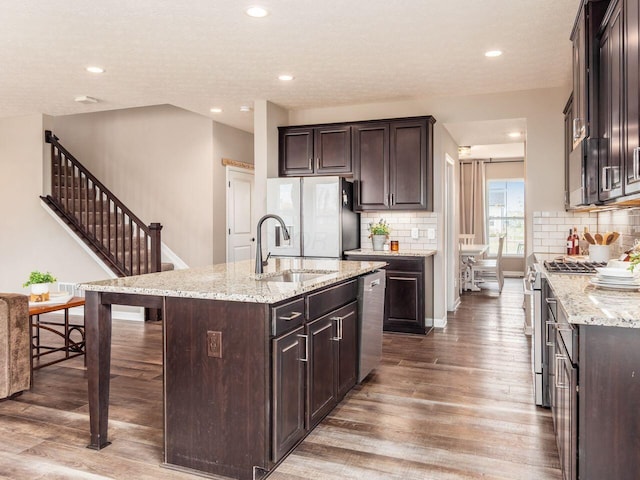 kitchen with light wood-style flooring, dark brown cabinets, a center island with sink, appliances with stainless steel finishes, and a sink