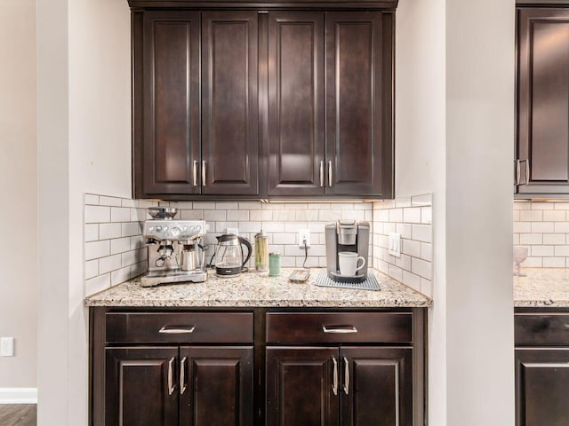 kitchen featuring baseboards, light stone countertops, dark brown cabinetry, and tasteful backsplash