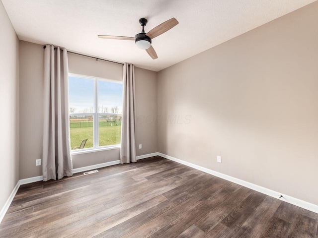 unfurnished room featuring a ceiling fan, dark wood-style floors, baseboards, and visible vents