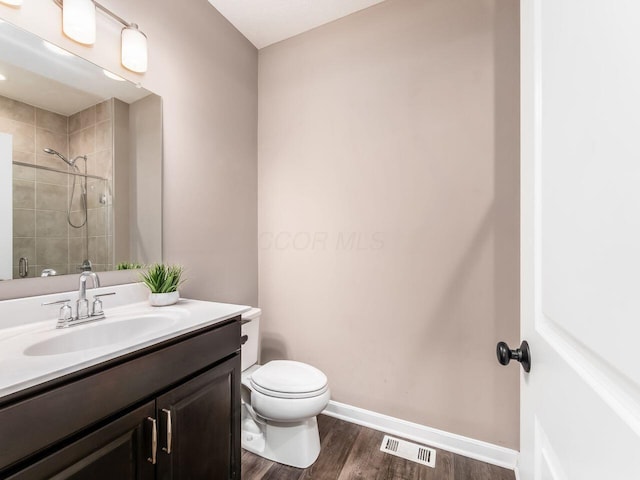 bathroom featuring visible vents, a tile shower, toilet, wood finished floors, and vanity