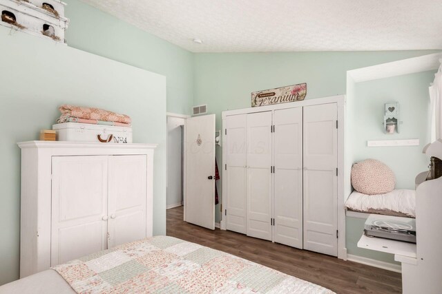 bedroom featuring a textured ceiling, a closet, visible vents, wood finished floors, and lofted ceiling